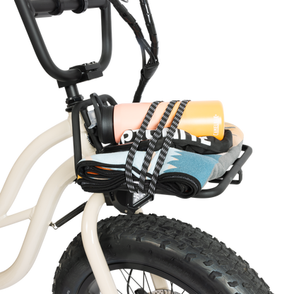 Murf Front Rack mounted on a cream-colored e-bike and loaded with a peach water bottle and colorful clothing items, demonstrating the use of the bungee straps for securing lightweight cargo.