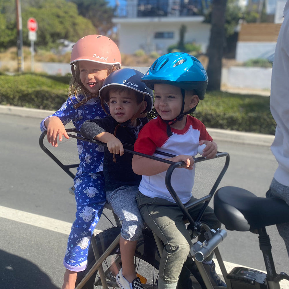 Lifestyle shot of three young riders seated safely within the Murf Cargo Carriage on a moving e-bike, clearly demonstrating the product's primary Problem-Solves: Safety and Cargo-Capacity for families.