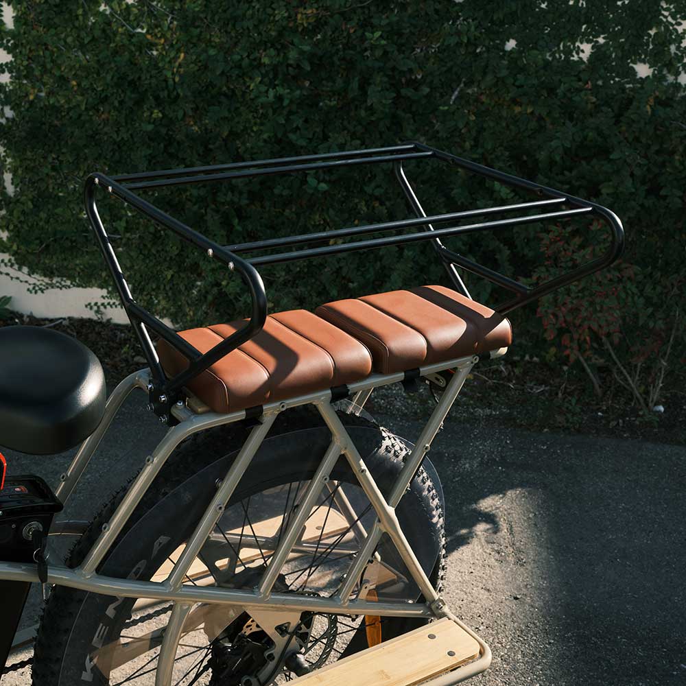 Brown Murf Cargo Seat Pad accessory installed on the extended rear cargo rack of a light-colored e-bike, featuring the Cargo Carriage installed